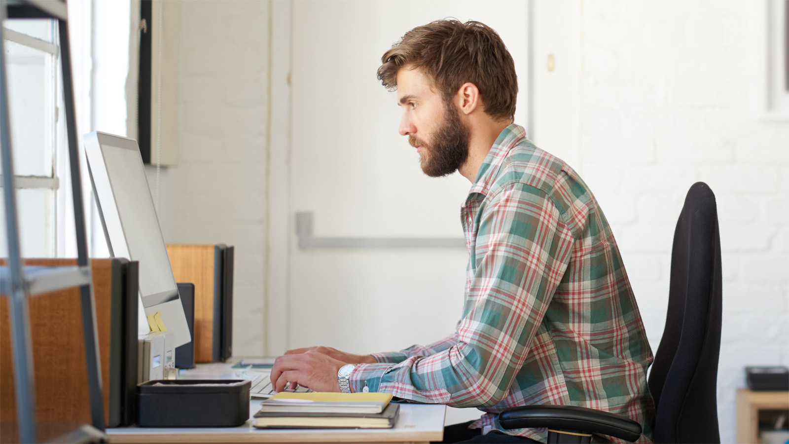 Man in plaid shirt typing on computer in remote office Man in plaid shirt typing on computer in remote office